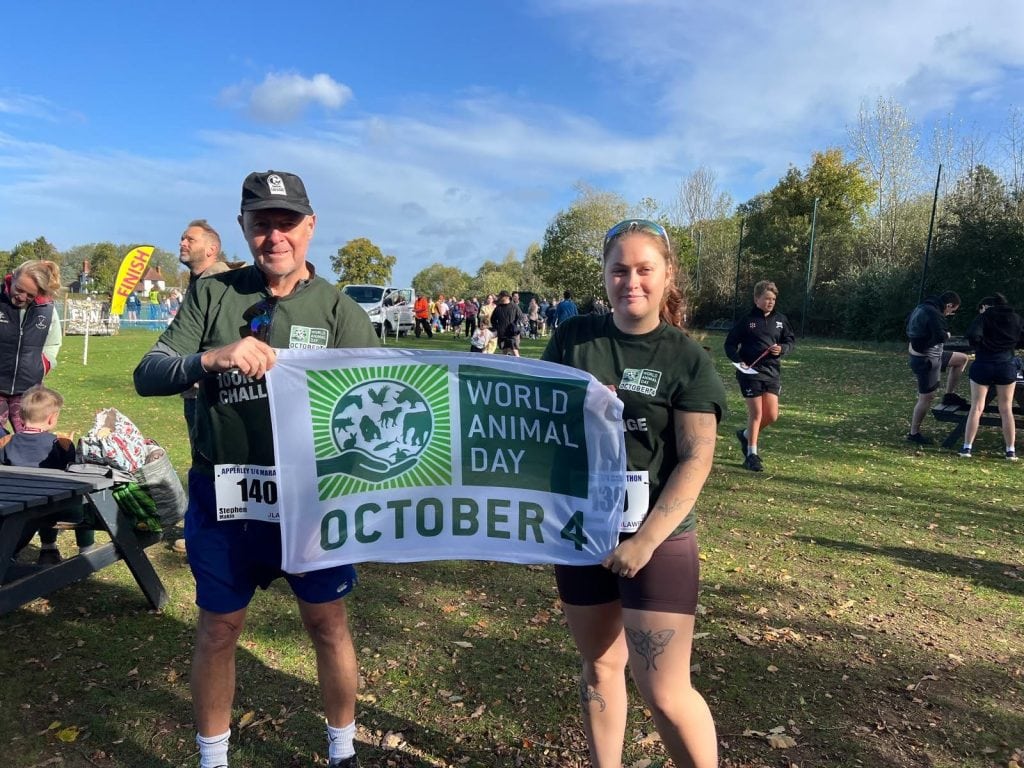 Two runners with World Animal Day t-shirts hold a World Animal Day banner that reads “October 4.”