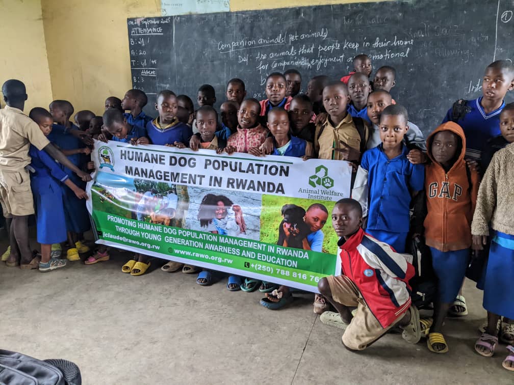 A group of Rwandan schoolchildren stand together in a classroom holding a banner that reads “Humane Dog Population Management in Rwanda.”