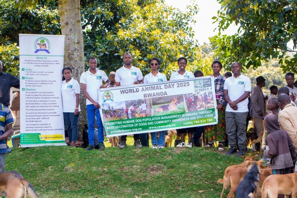 Members of the Rwanda Animal Welfare Organization (RAWO) standing outdoors holding a banner for World Animal Day 2025, promoting dog vaccination and animal welfare awareness, surrounded by dogs.